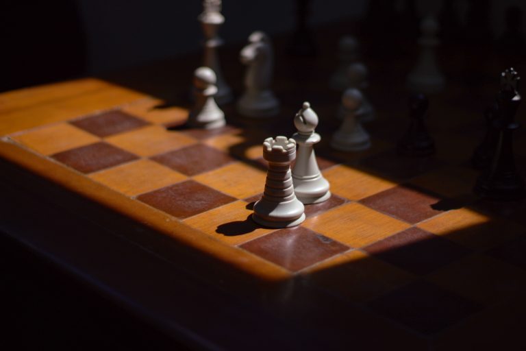 White bishop and rook on a chessboard with white pieces in the background.